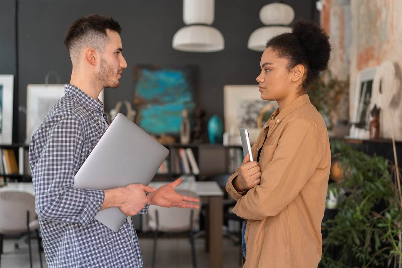 Man and Woman Having a Conversation while Holding Their Laptop